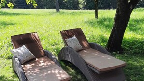 Two outdoor lounge chairs with cushions and a table, placed on a grassy area with trees in the background. - Apartment in Neuhaus Near Petzen Ski Area (Neuhaus)