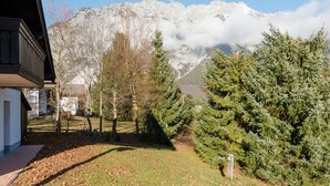 A mountain view with snow-capped peaks, a building with a balcony, and a well-maintained lawn with trees. - Quaint Holiday in Gröbming near Skiing (Groebming)