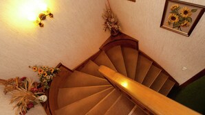 Un escalier en colimaçon avec une rampe en bois, un luminaire fixé au mur et une œuvre d’art florale encadrée.