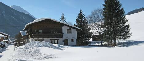 A snow-covered building with a wooden facade, a balcony, and a mountain backdrop.