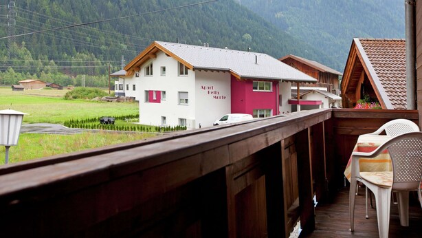 Un balcon en bois offrant une vue sur une montagne et sur un immeuble portant l’inscription « Aparth Bella Monte ».