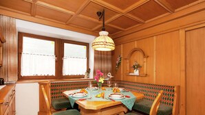 Une cuisine chaleureuse avec des meubles en bois, une table à manger pour quatre personnes et un banc doté d’assises rembourrées vertes.
