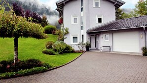 A two-story building with a grey facade, a tiled roof, and a paved driveway leading to a garage.