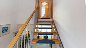 A staircase with wooden steps and blue carpet runners, leading to a room with a door and a light fixture on the ceiling.