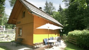 En træhytte med en patio, der indeholder et bord, stole, en bænk og en stor parasol.