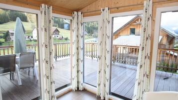 Una habitación con ventanas amplias, terraza de madera y vistas a una casa de madera.