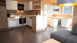 A modern kitchen with white cabinets, a central island, and a dining area with a table and chairs. - Wooden Chalet in Hohentauern With Sauna (Hohentauern)