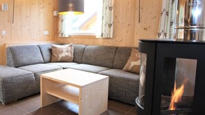 A cozy living room with a grey sectional sofa, a wooden coffee table, and a wood-burning stove. - Wooden Chalet in Hohentauern With Sauna (Hohentauern)