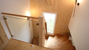 A wooden staircase with a glass handrail, a door with a metal handle, and a window with a view of greenery outside. - Wooden Chalet in Hohentauern With Sauna (Hohentauern)