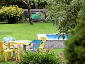 A garden with a small pool, a wooden deck, and colorful plastic chairs. - Apartment in Waidring Near Pillerseetal Ski Area (Waidring)