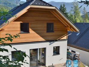 Ein zweistöckiges Holzhaus mit geneigtem Dach, großen Fenstern und Bergblick.