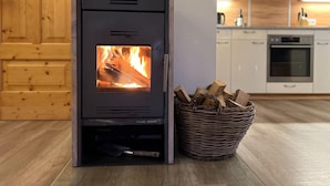 A modern kitchen with a wood-burning stove, a basket of firewood, and wooden cabinets. - Chalet Only 200 m From ski Lift With Sauna (Bad Kleinkirchheim)