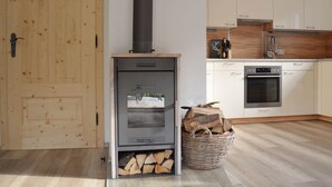 A modern kitchen with a wood-burning stove, wooden cabinets, and a basket of firewood. - Chalet Only 200 m From ski Lift With Sauna (Bad Kleinkirchheim)