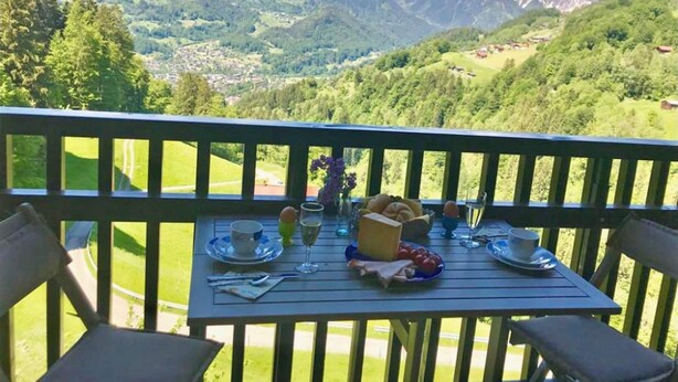 A dining table with plates, glasses, and food items, set on a balcony with a mountain view. - Cozy Apartment in Schruns Vorarlberg near Ski Area Montafon (Schruns)
