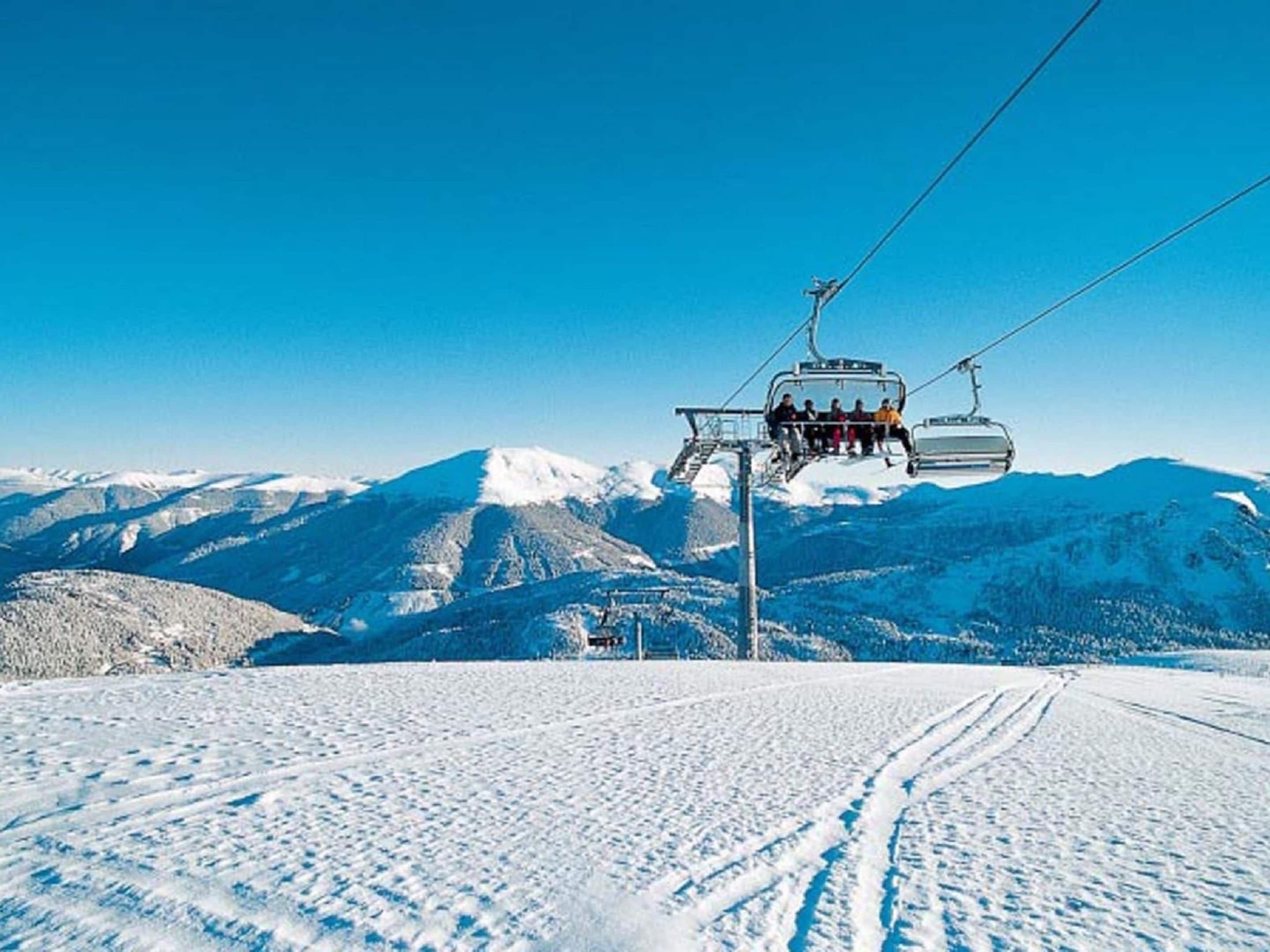 Un teleàsqueic amb viatgers, muntanyes cobertes de neu i un cel serè.