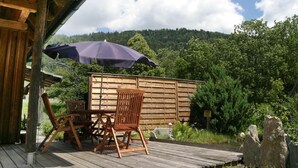 A wooden deck with a table and chairs, an umbrella, and a wooden fence with a view of a forested hillside. - Chalet in Einach Near Ski Slopes (Stadl-Predlitz)