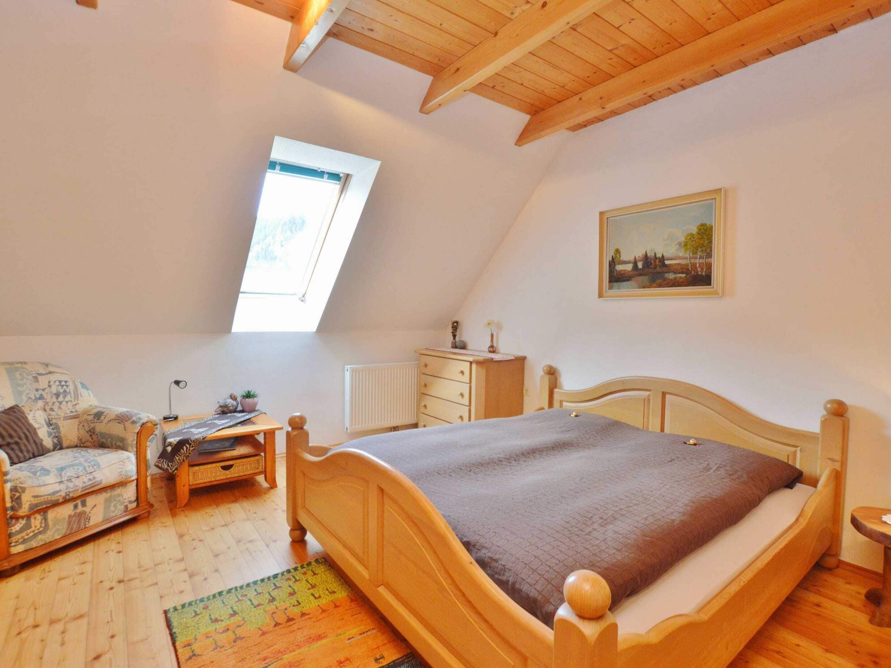 A cozy bedroom with a sloped ceiling, a skylight, a wooden bed, a small desk, a chair, and a radiator.