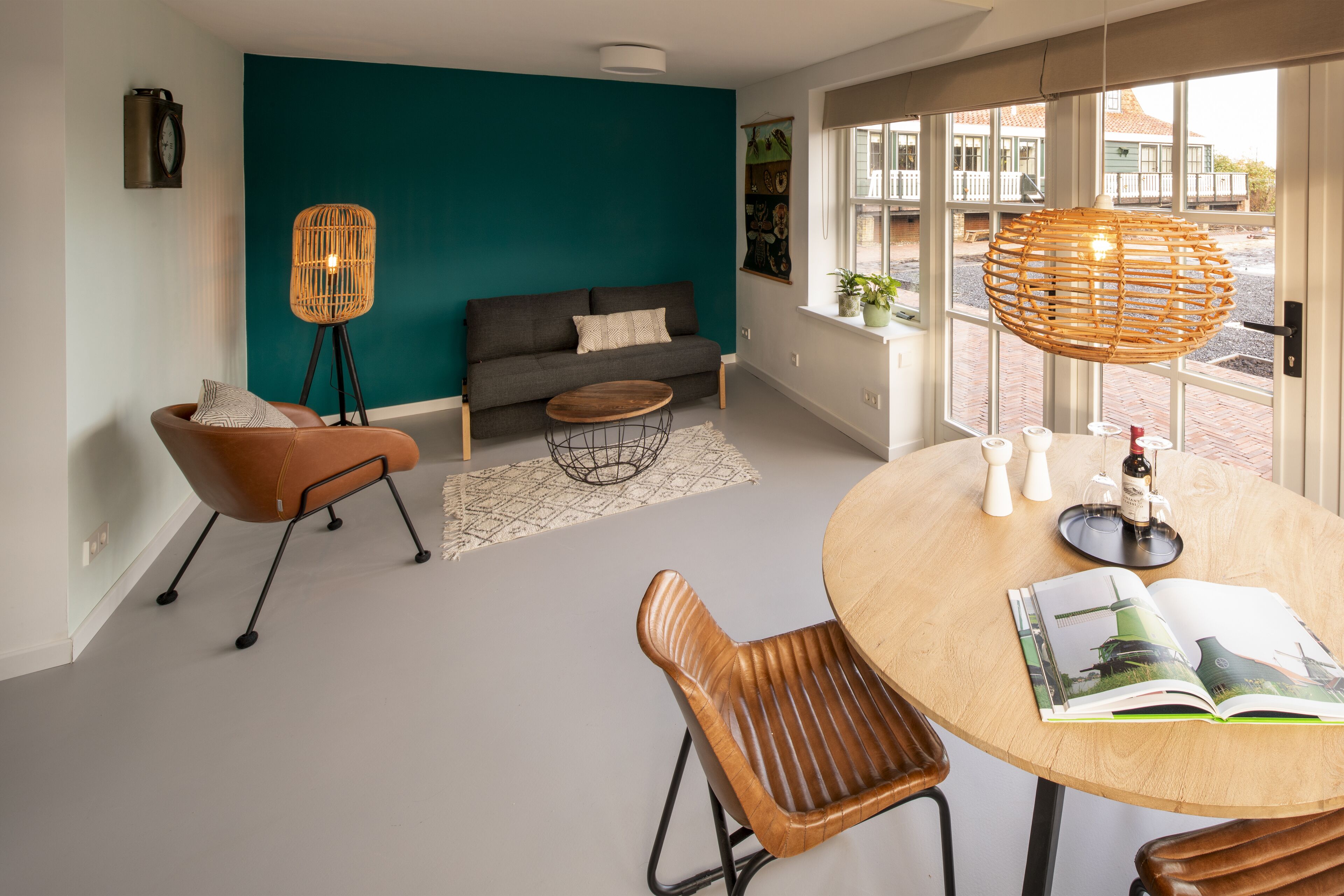A modern living room with a teal accent wall, a sofa, a coffee table, and a dining table with chairs.