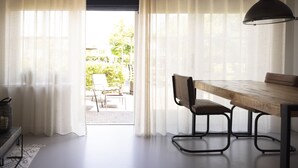 A room with a wooden dining table, a chair, and a lamp. There is a window with sheer curtains, and a view of the outside. - B&B Saenliefde (Wormer)