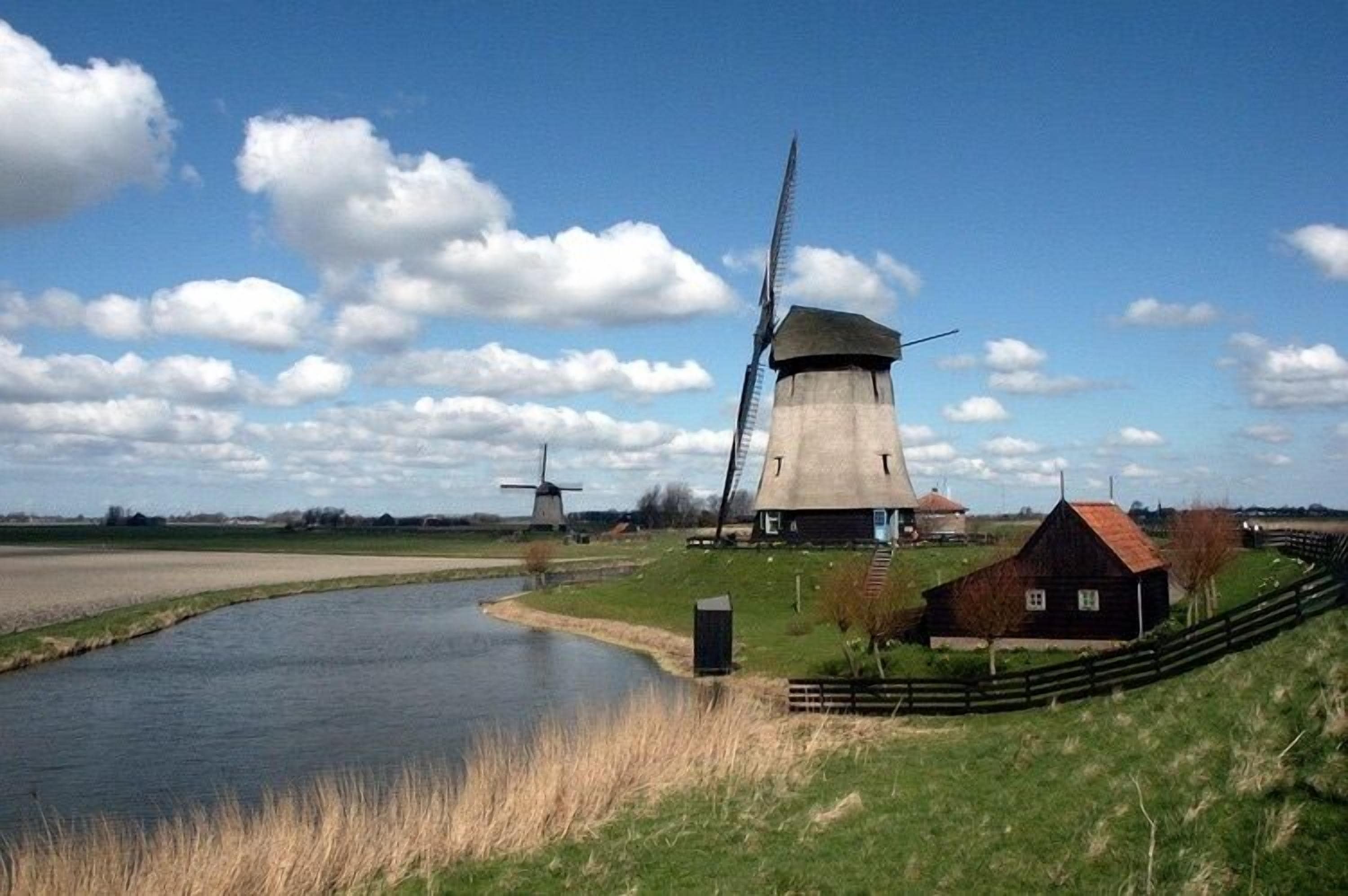 A windmill, a water canal, and a small building with a red roof.