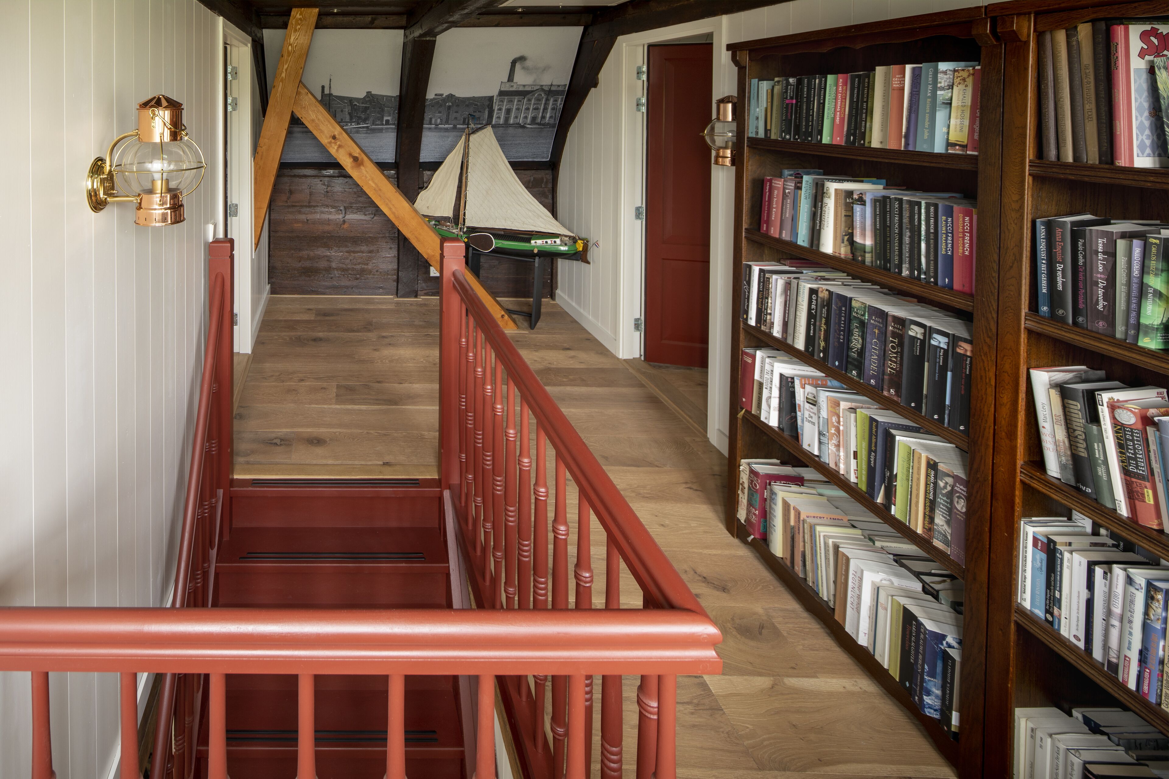 Un escalier avec une rampe rouge menant à un palier où se trouve une bibliothèque remplie de livres.