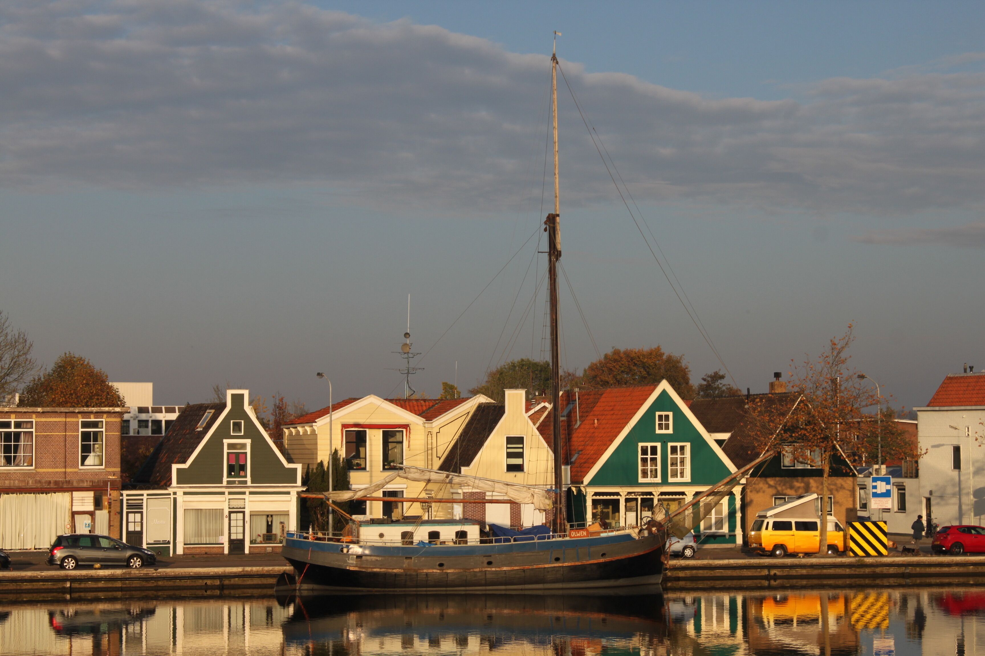 A waterfront scene with a boat docked near buildings with distinct architectural styles, including a green house with a red roof.