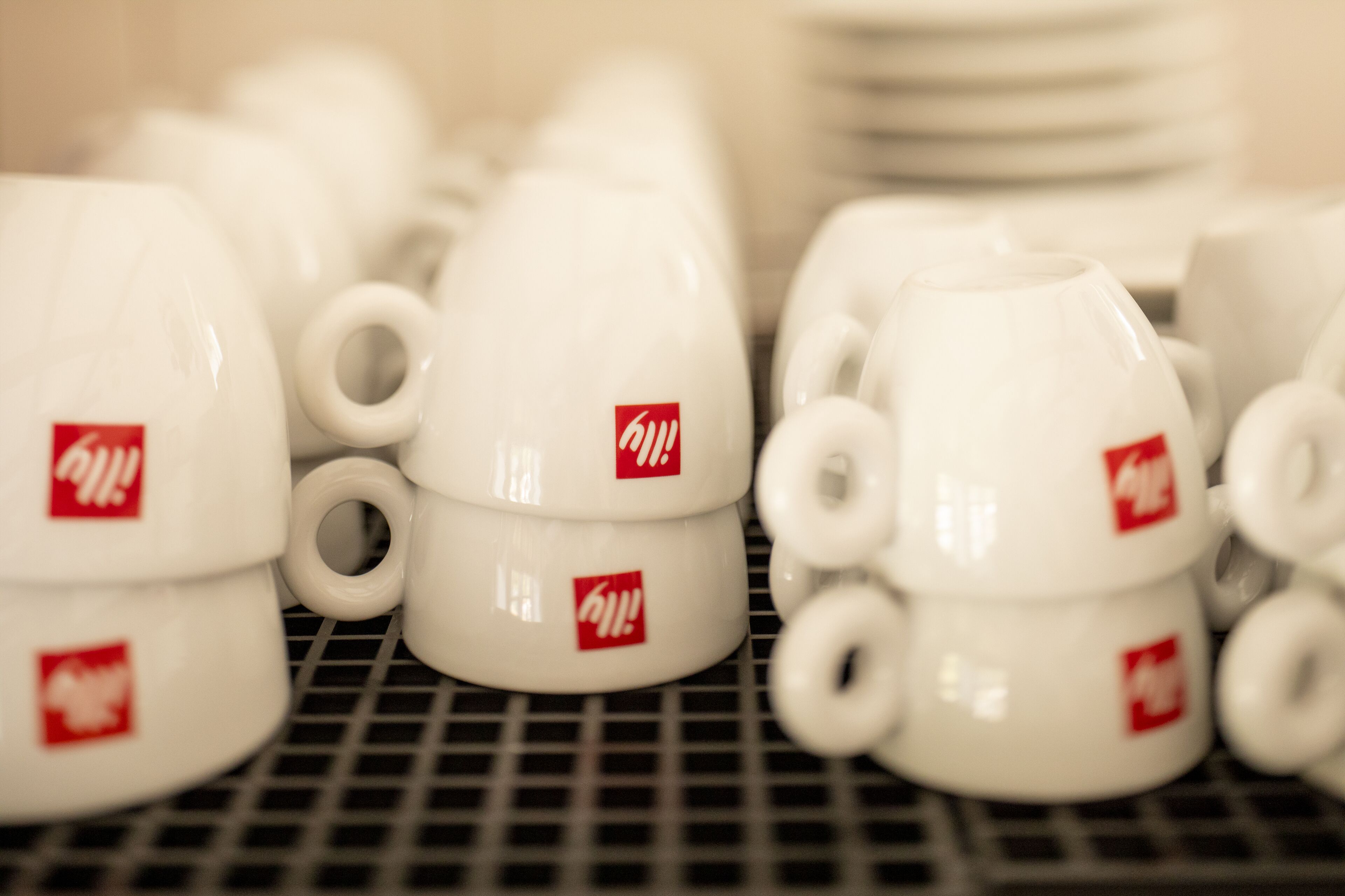A collection of white ceramic mugs with red logos, arranged on a metal rack.