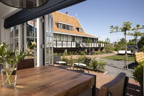 An outdoor seating area with a wooden table and chairs, a potted plant, and a view of a house with a sloped roof and white railings. - B&B Saenliefde (Wormer)