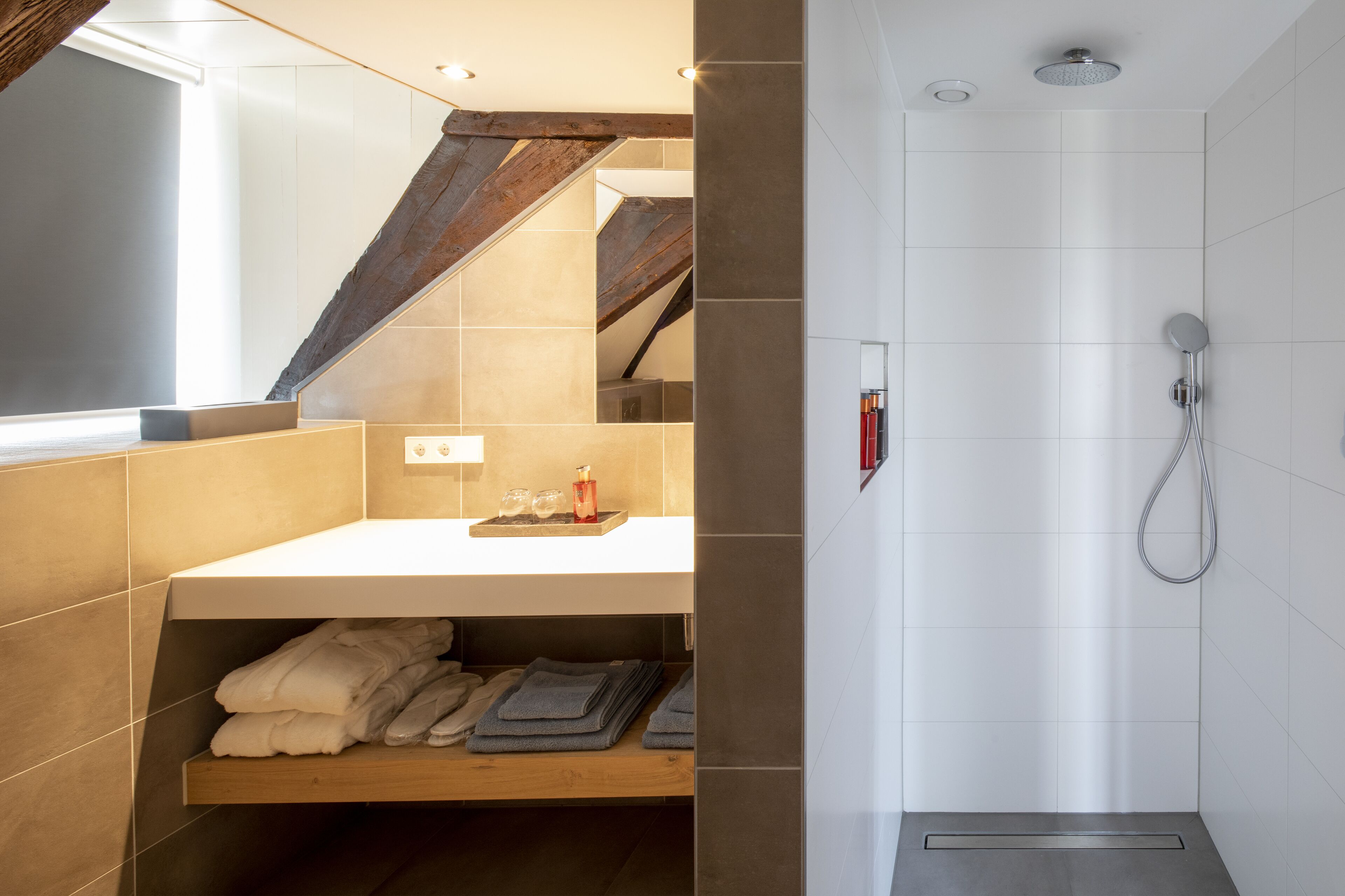 Un bany modern amb una prestatgeria de fusta plena de tovalloles, un lavabo blanc amb un safata, i una dutxa amb un braç de dutxa portàtil.