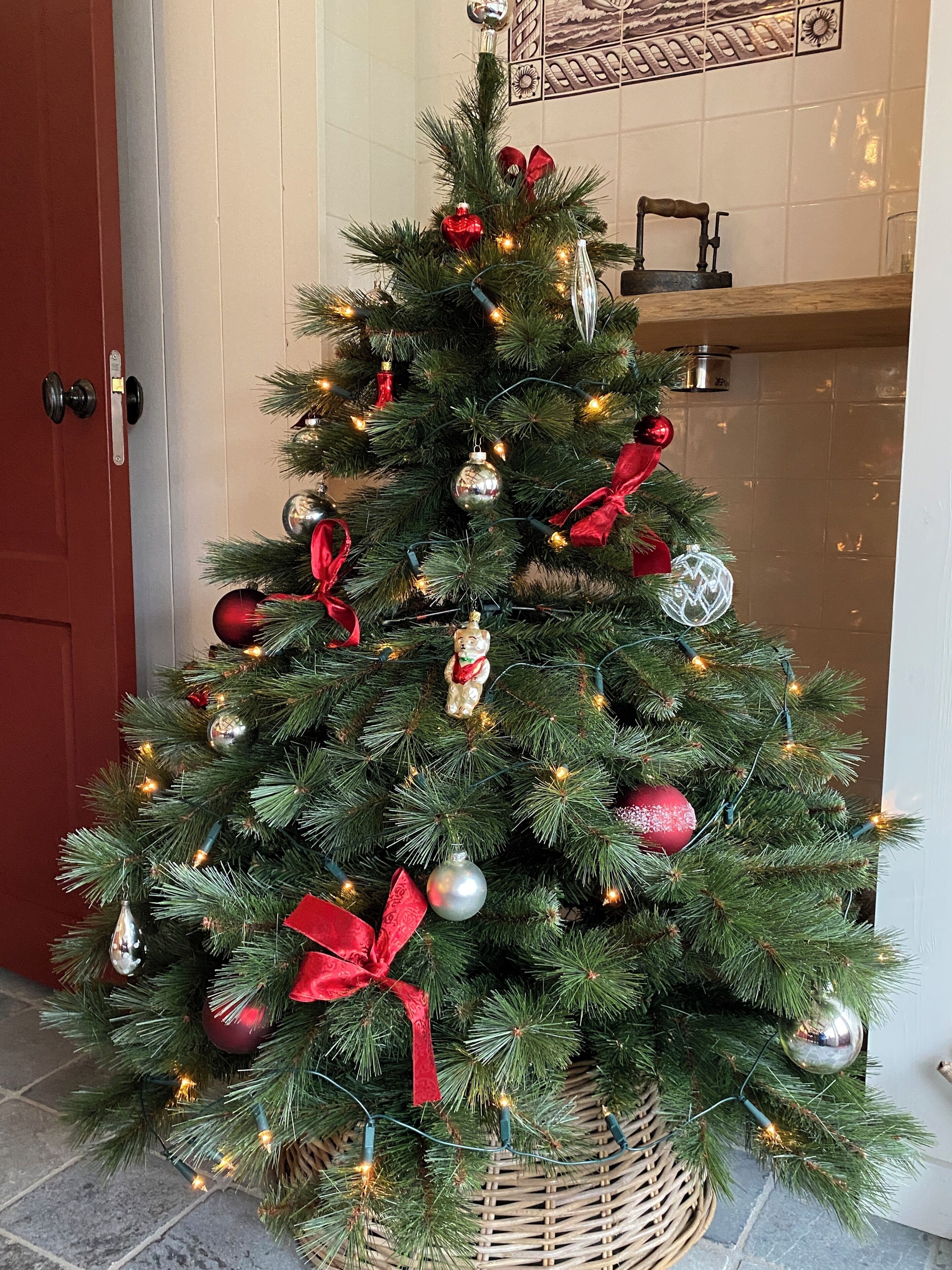 A Christmas tree with red and silver ornaments and lights, placed in a wicker basket.
