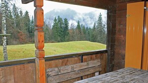 Un banc et une table en bois, situés dans un chalet avec vue sur un champ verdoyant et des montagnes.