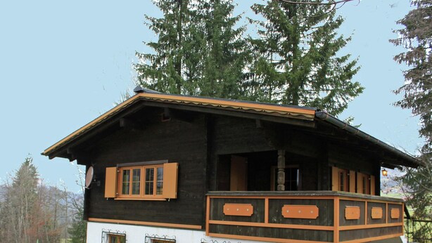 Une cabane en bois dotée d’un balcon, de grandes fenêtres et d’un petit espace porche.
