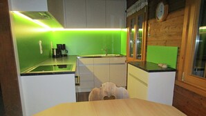 Une cuisine compacte avec un plan de travail éclairé de couleur verte, une table à manger en bois et une horloge au mur.