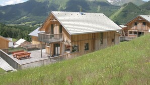 A wooden chalet with a balcony, set against a mountainous backdrop. - Comfortable Chalet in Hohentauern with Whirlpool near City Center (Hohentauern)