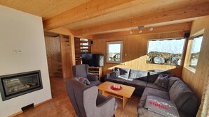 A cozy living room with a fireplace, a large sofa, a television, and wooden walls. - Comfortable Chalet in Hohentauern with Whirlpool near City Center (Hohentauern)