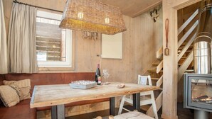 Ein gemütliches Holzinnere mit Esstisch, Bankbestuhlung, einer Pendelleuchte, einem Kamin und einer Treppe.