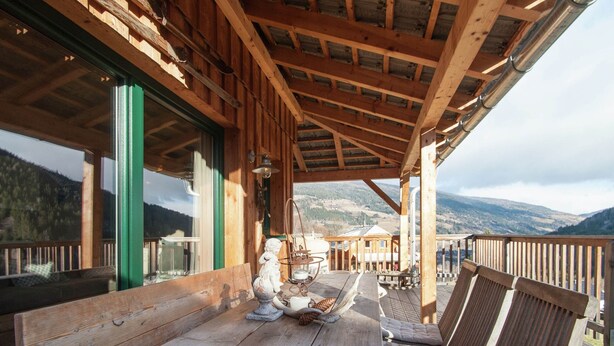 Eine Holzterrasse mit Tisch und Stühlen, mit Blick auf eine gebirgige Landschaft.