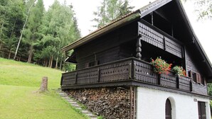 Perinteinen puinen alppimaja, jossa on parveke, kiviporras ja valkoinen ulkoseinä.