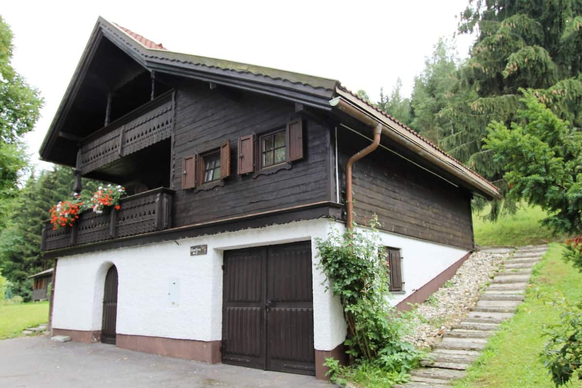 Een klassiek chalet met balkon, garage en een trap naar de ingang.