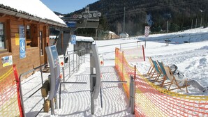 Eine Liftstation mit Holzbauten, schneebedecktem Boden und einem eingezäunten Bereich, im Hintergrund ist eine Sesselliftbahn zu sehen.
