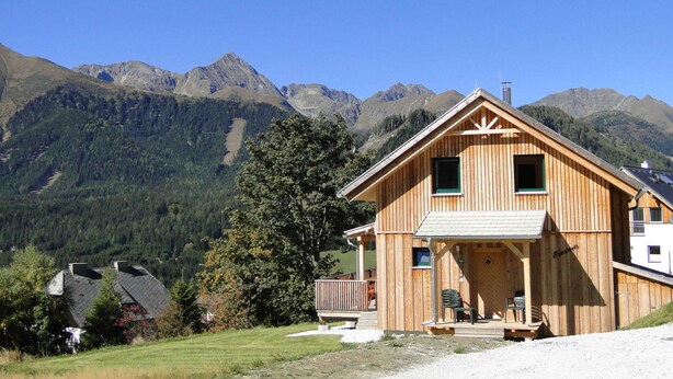 Eine Holzhütte mit Balkon, eingebettet in eine gebirgige Landschaft.
