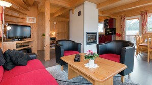 Ein gemütliches Holzhaus-Interieur mit einem Wohnbereich, ausgestattet mit einer Couch, zwei Sesseln, einem Holztisch und einem Flachbildfernseher.