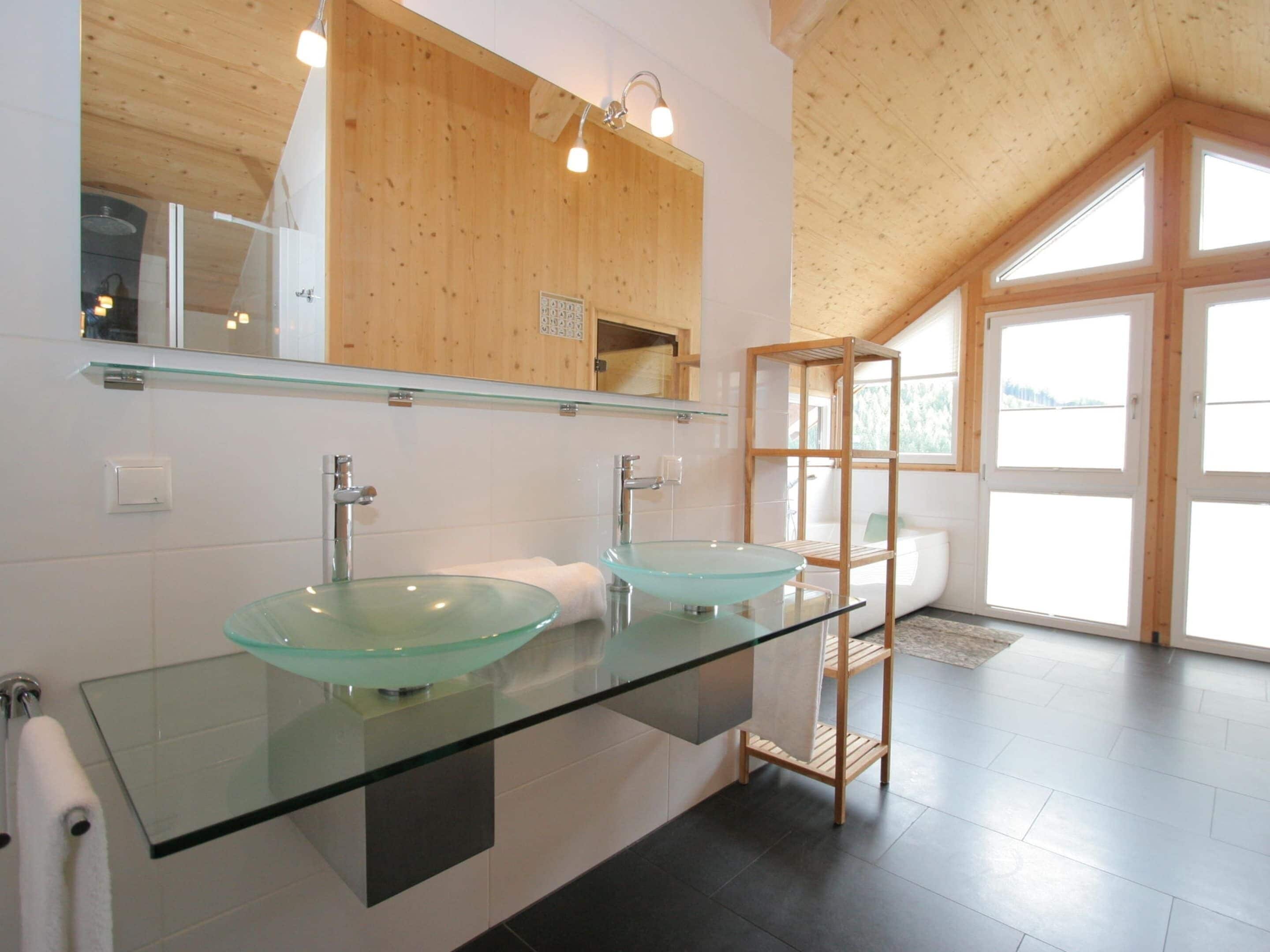 A modern bathroom with two glass sinks, wooden cabinets, and a large window providing natural light.