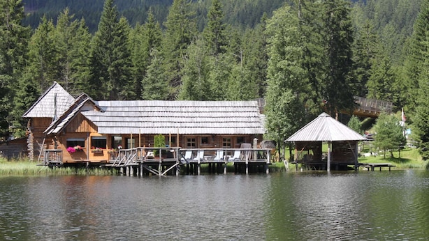 Una cabaña de madera con un muelle que se adentra en un lago, rodeada de un bosque denso.