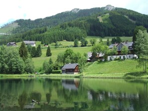 A lakeside village with traditional houses, a wooden cabin, and a mountain backdrop.