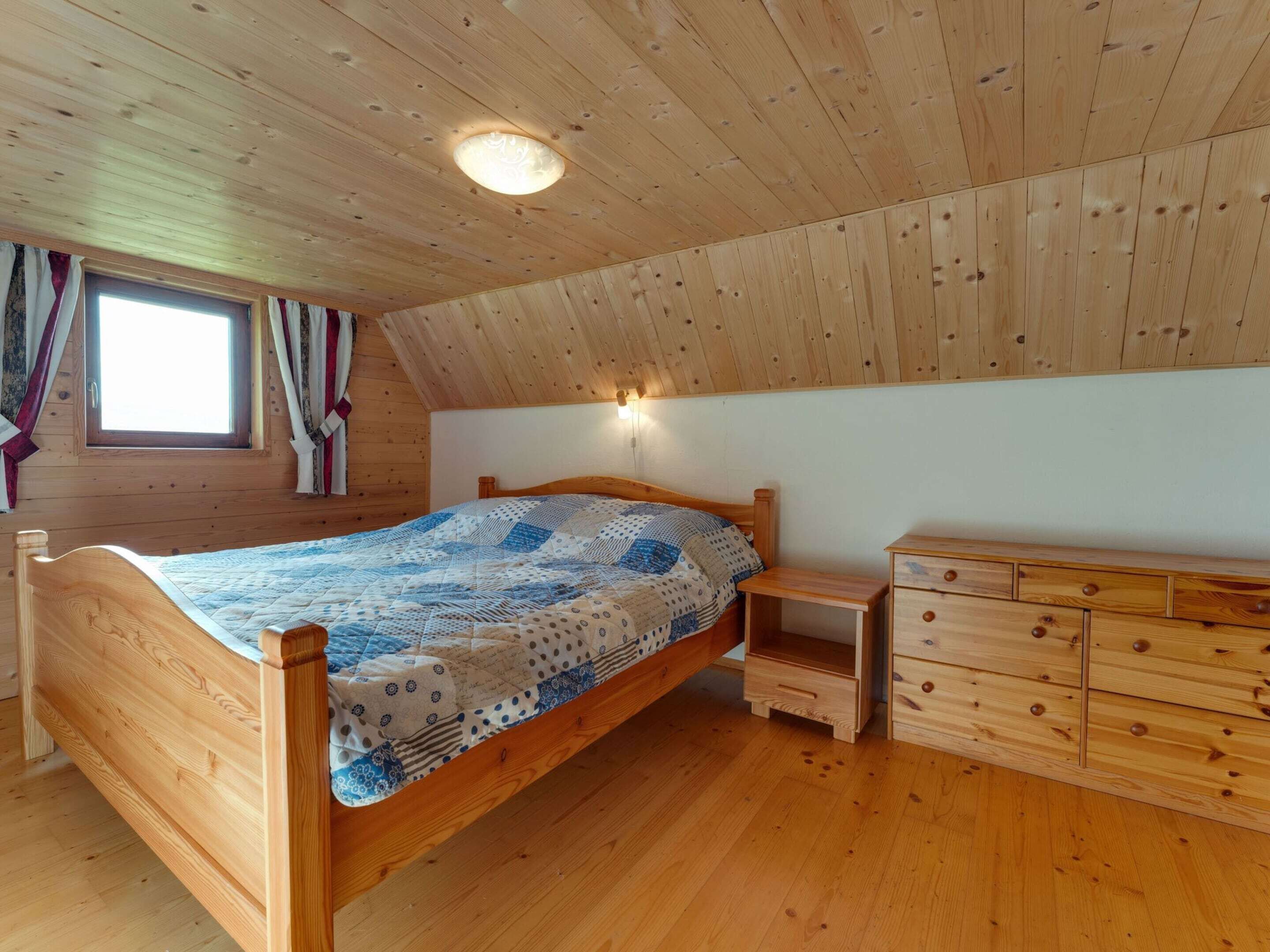 Una habitación con paneles de madera, una cama, un aparador y una ventana con cortinas.