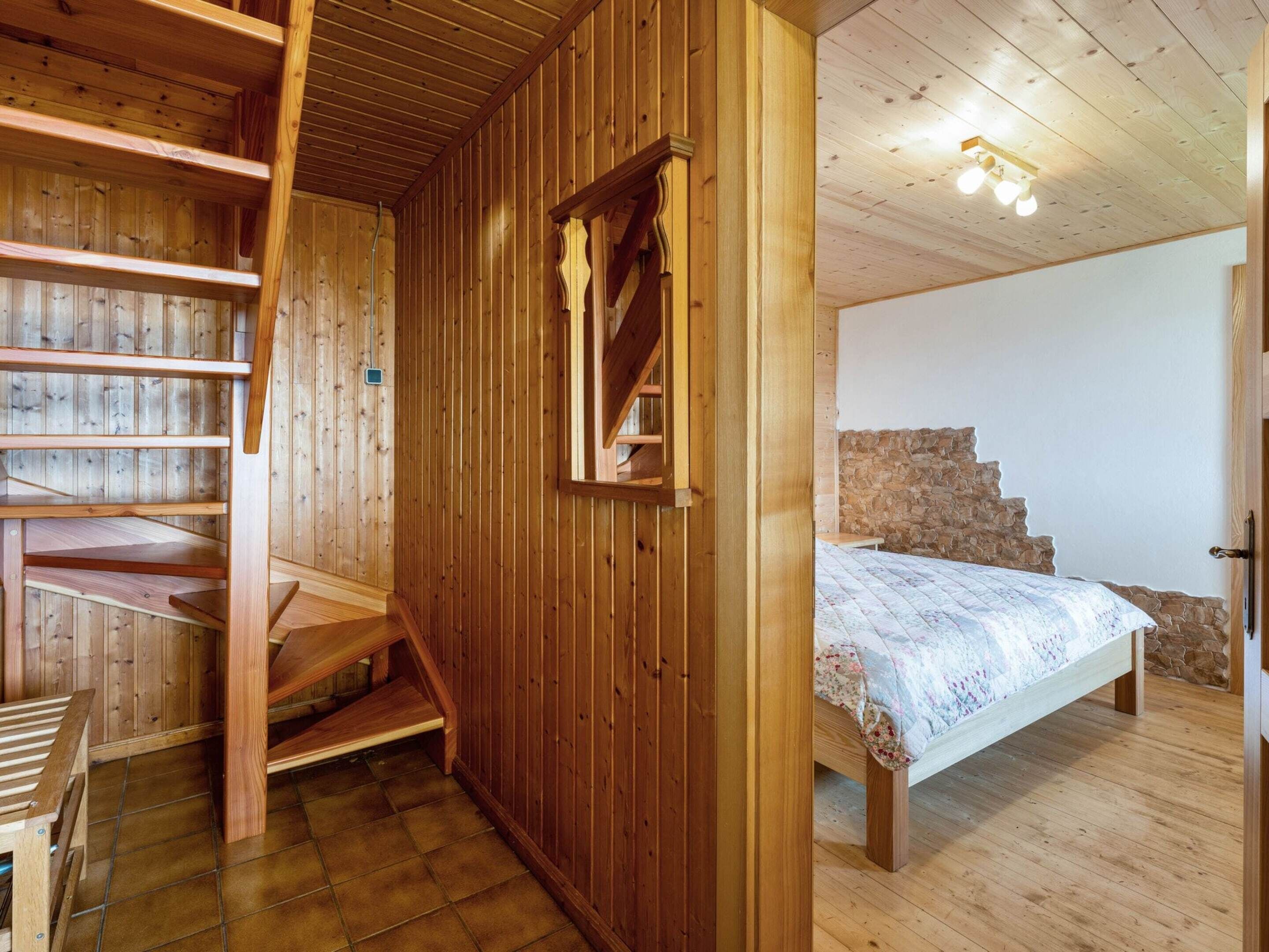 Ein Holzinnenraum mit einem Bett, einer Treppe und einer Steinwand.