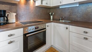 Una cucina moderna con mobili bianchi, una cappa in acciaio inossidabile, forno integrato, macchina del caffè e lavello.