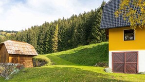 Paesaggio rurale con una stalla in legno e una casa gialla con tetto in tegole.