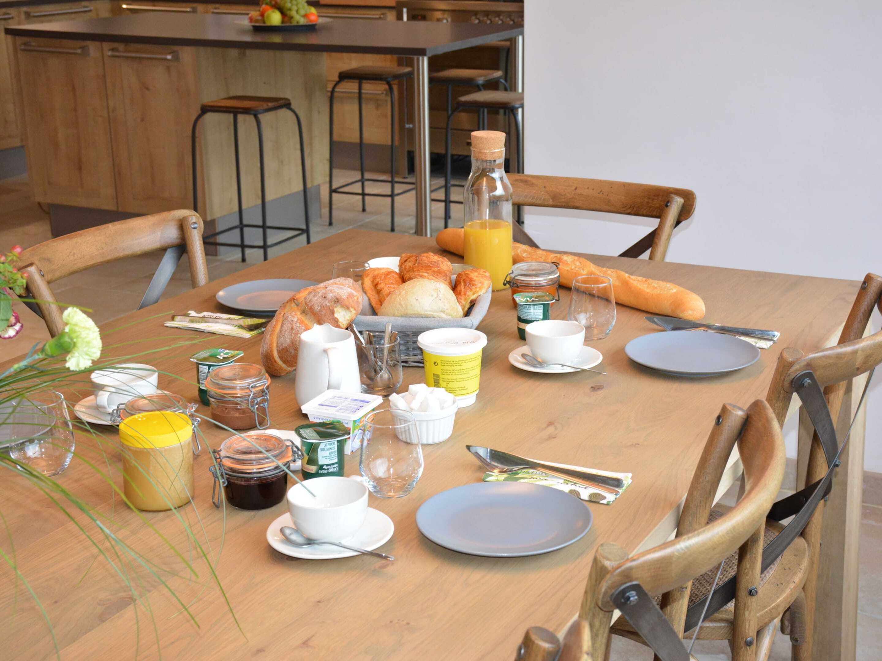 A breakfast table set with bread, pastries, a bottle of juice, and various breakfast items.